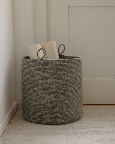 Large green melange basket holding rolled papers in a softly lit room.
