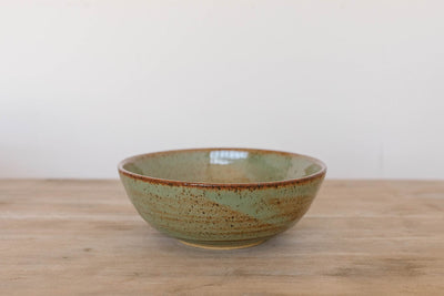 Green handmade ceramic ramen bowl on a wooden surface with a white background