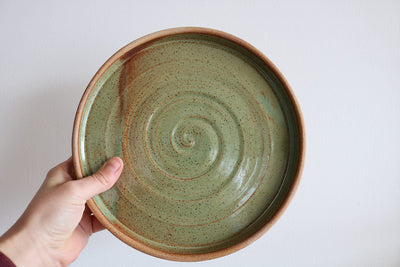 Hand holding a ceramic plate with a spiral design on a white background
