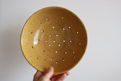 Hand holding a yellow ceramic colander with holes on a white background