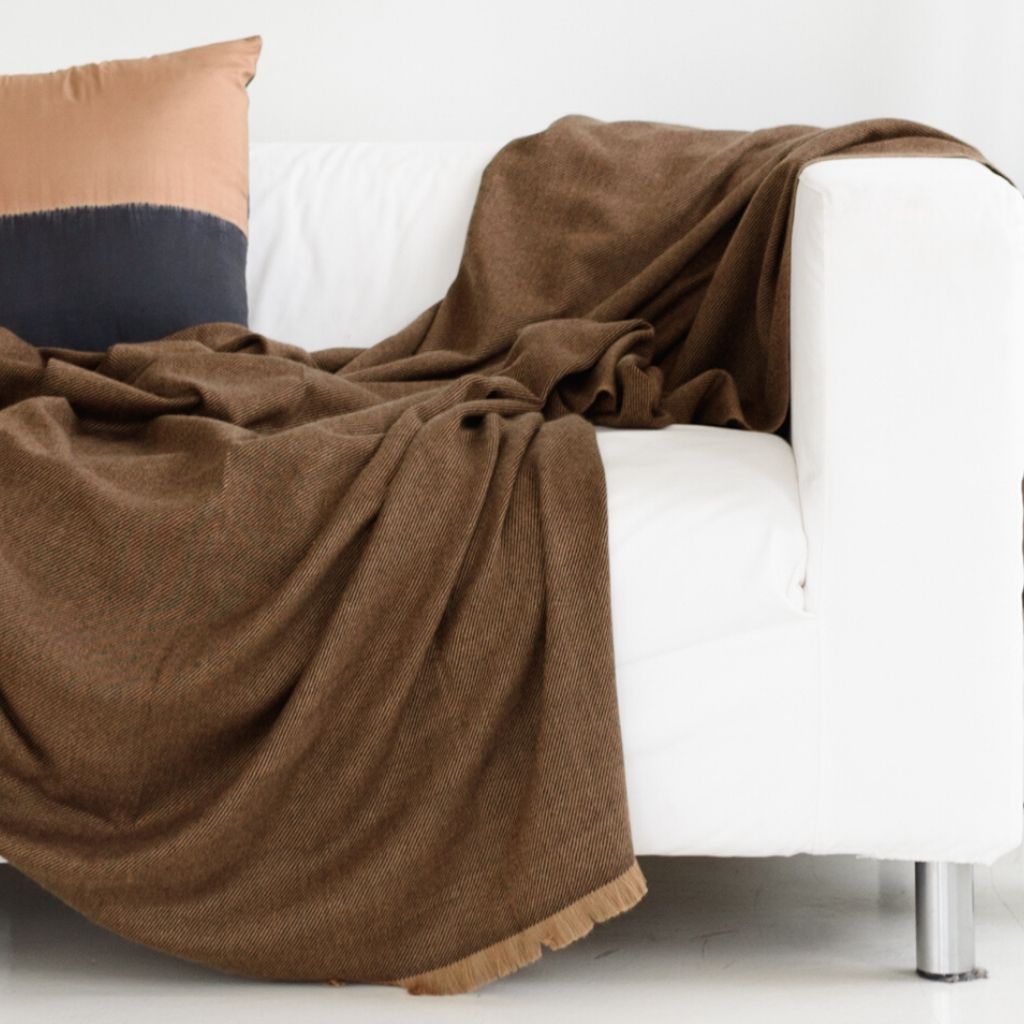 Hay Brown handwoven throw spread casually over a white sofa with neutral and navy accent pillows