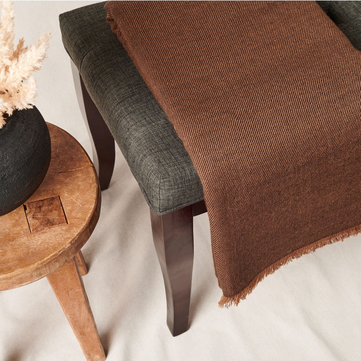 Close angled view of the Hay Brown throw draped over a charcoal chair beside a rustic wood stool