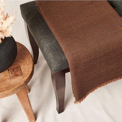 Close angled view of the Hay Brown throw draped over a charcoal chair beside a rustic wood stool