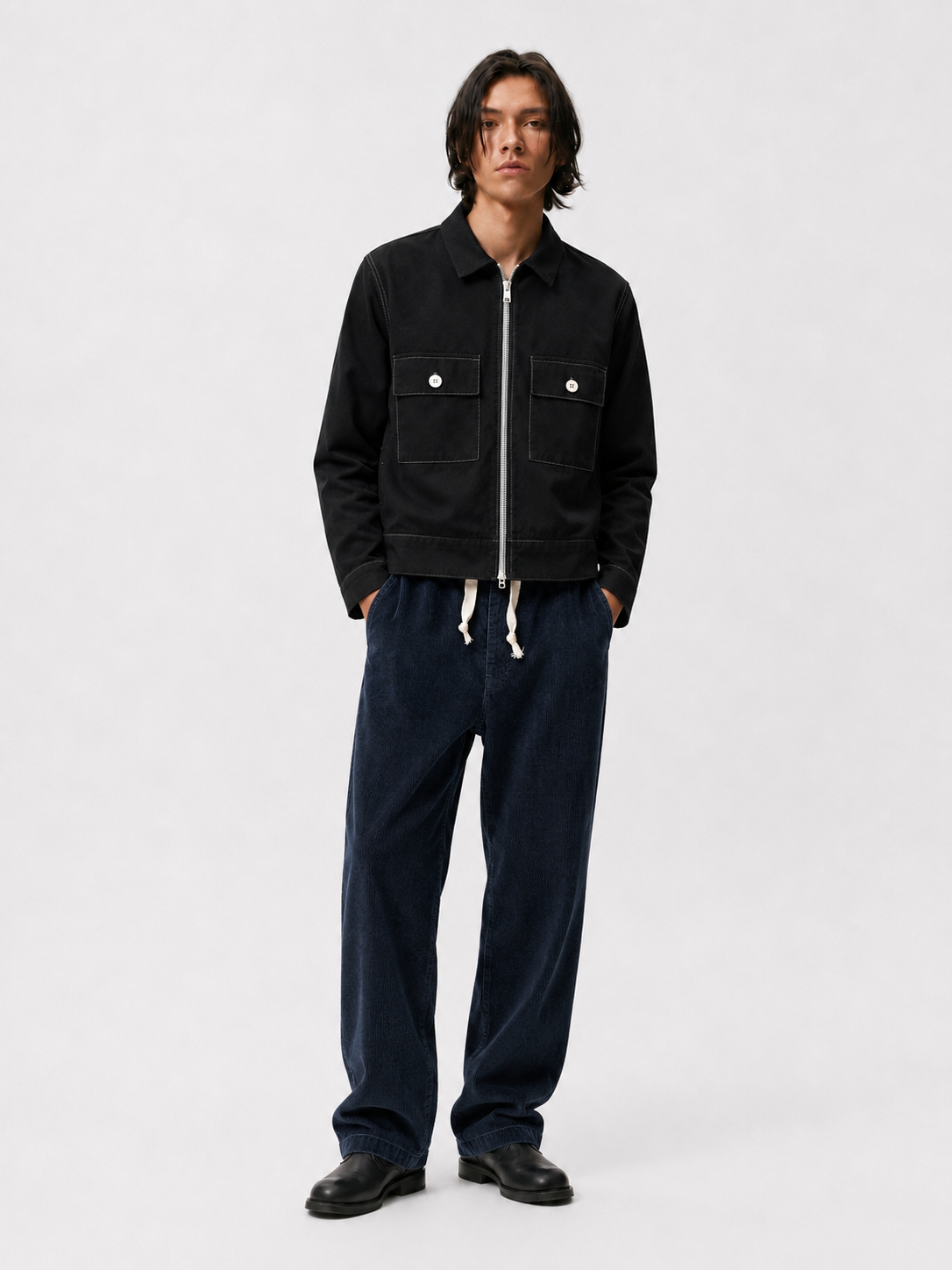 Model wearing navy corduroy Paddington pants with a white drawstring, black jacket, and black shoes.