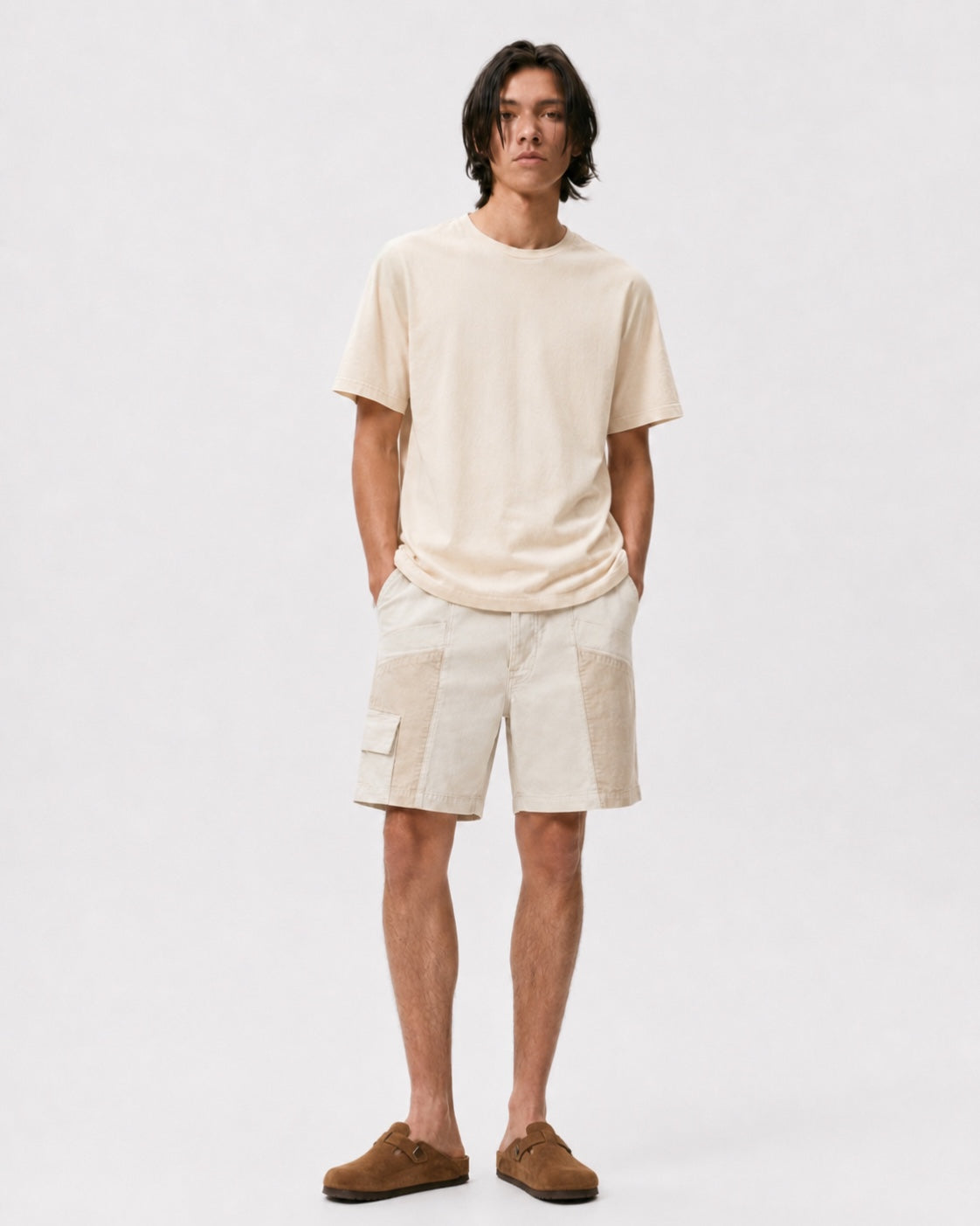 Model wearing cream Trek Shorts with tonal utility panels and a side cargo pocket, paired with a cream T-shirt and brown slip-on shoes.