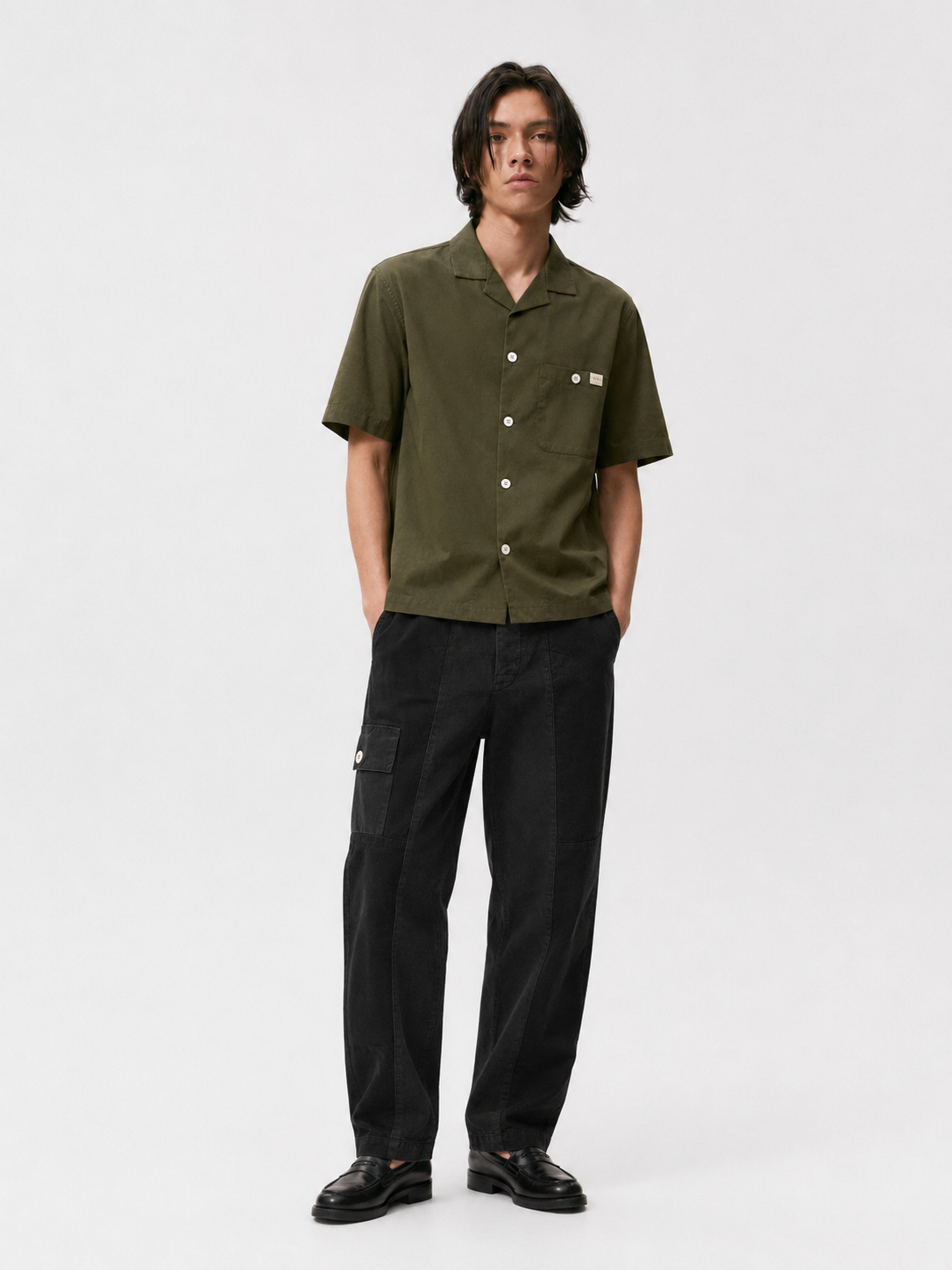 Model wearing black Trek pants with tonal utility panels and a side cargo pocket, paired with an olive short-sleeve shirt.