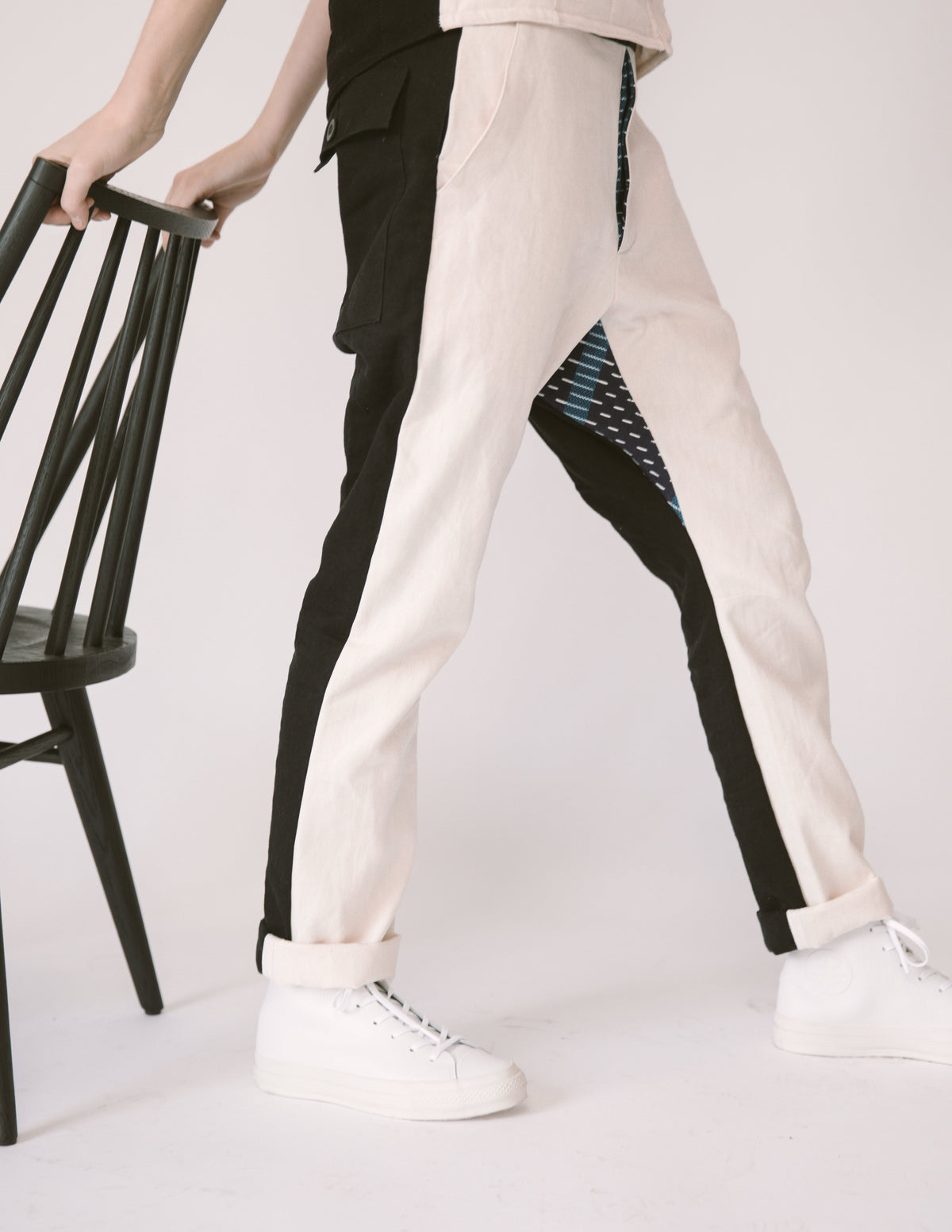 Cropped studio view of two models wearing cream and black Vet Chinos with cuffed hems and white sneakers beside a black chair.