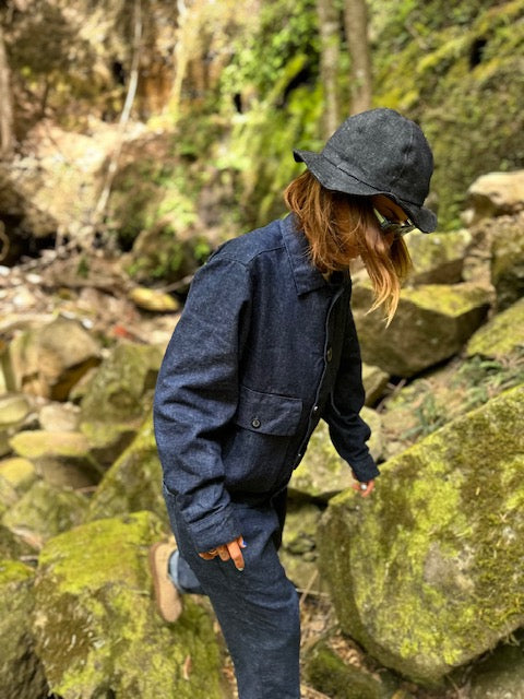 Model wearing a dark indigo hemp-denim Studio Coat and matching pants while climbing through a mossy forest.