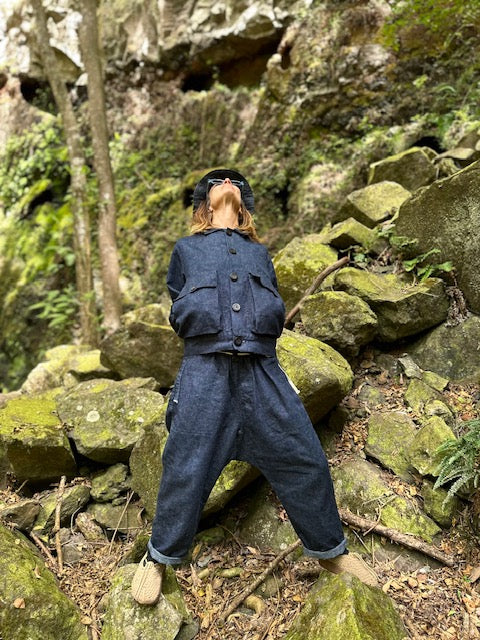 Model wearing the indigo Studio Coat and matching loose pants among moss-covered rocks.