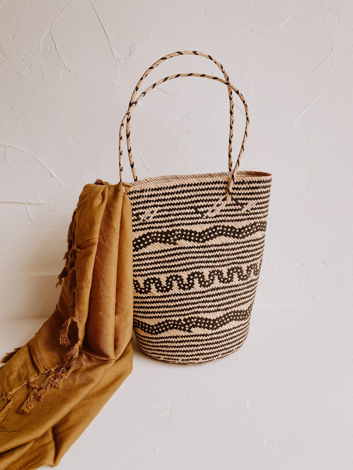 Village Thrive Praya Day Bag, natural rattan with black wave pattern, hanging on a wall hook.
