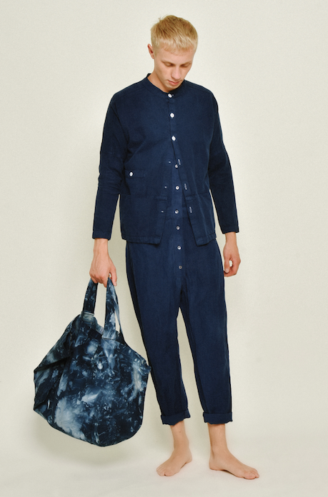 Barefoot model wearing a navy Raj corduroy coat with matching pants while holding a blue patterned bag.