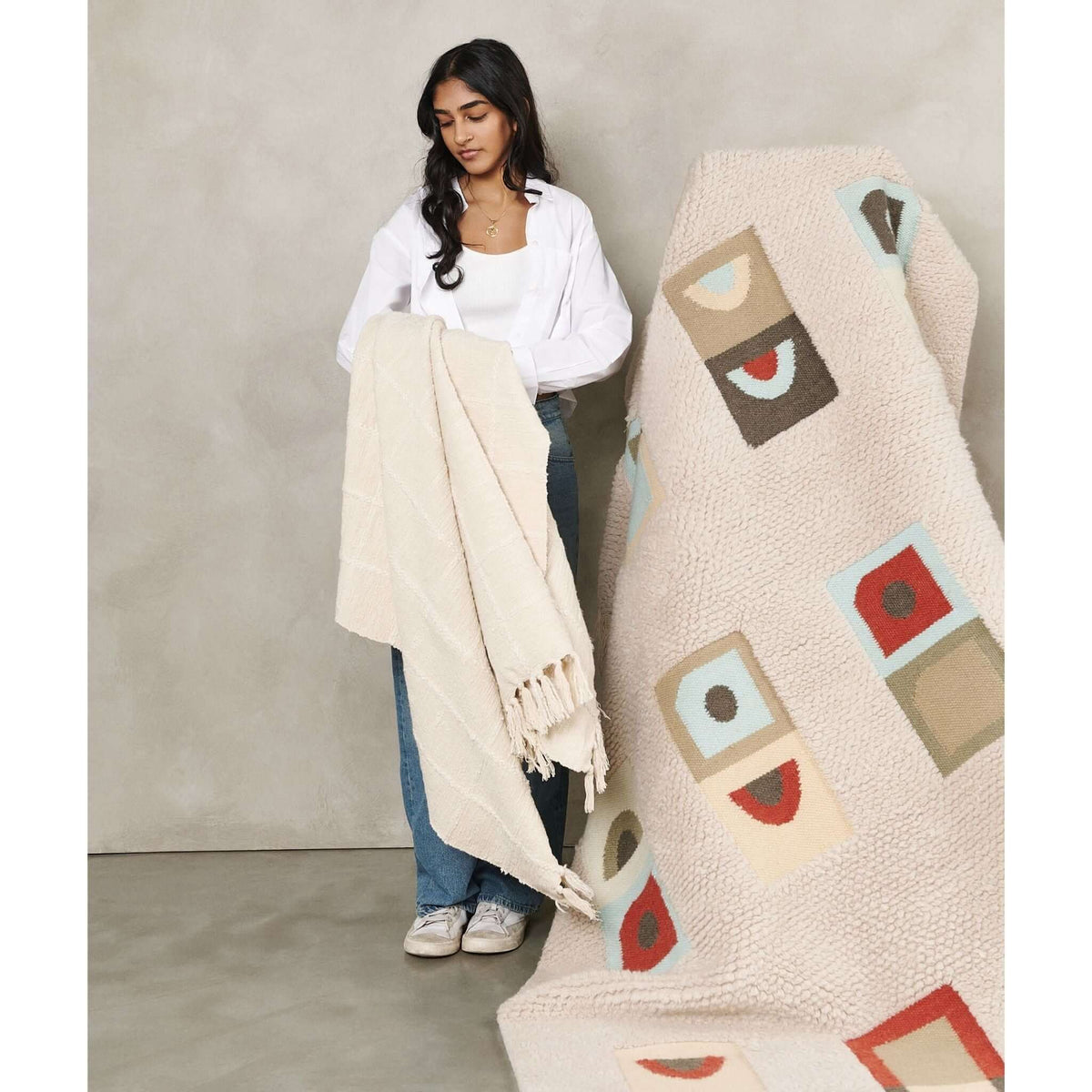 Woman holding the Sea Shell White throw in front of a multicolored geometric rug to show its neutral tone and fringed border