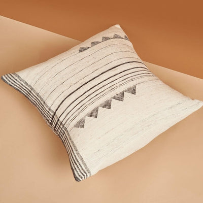 White and black patterned pillow styled diagonally on a warm tan surface.