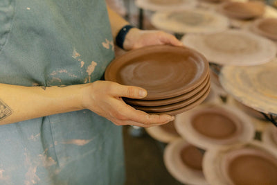 Potter holding stacked handmade earthenware small plates in studio