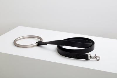 Black Lumi Leash coiled on a raised white display block with its polished clasp and large silver ring handle visible.