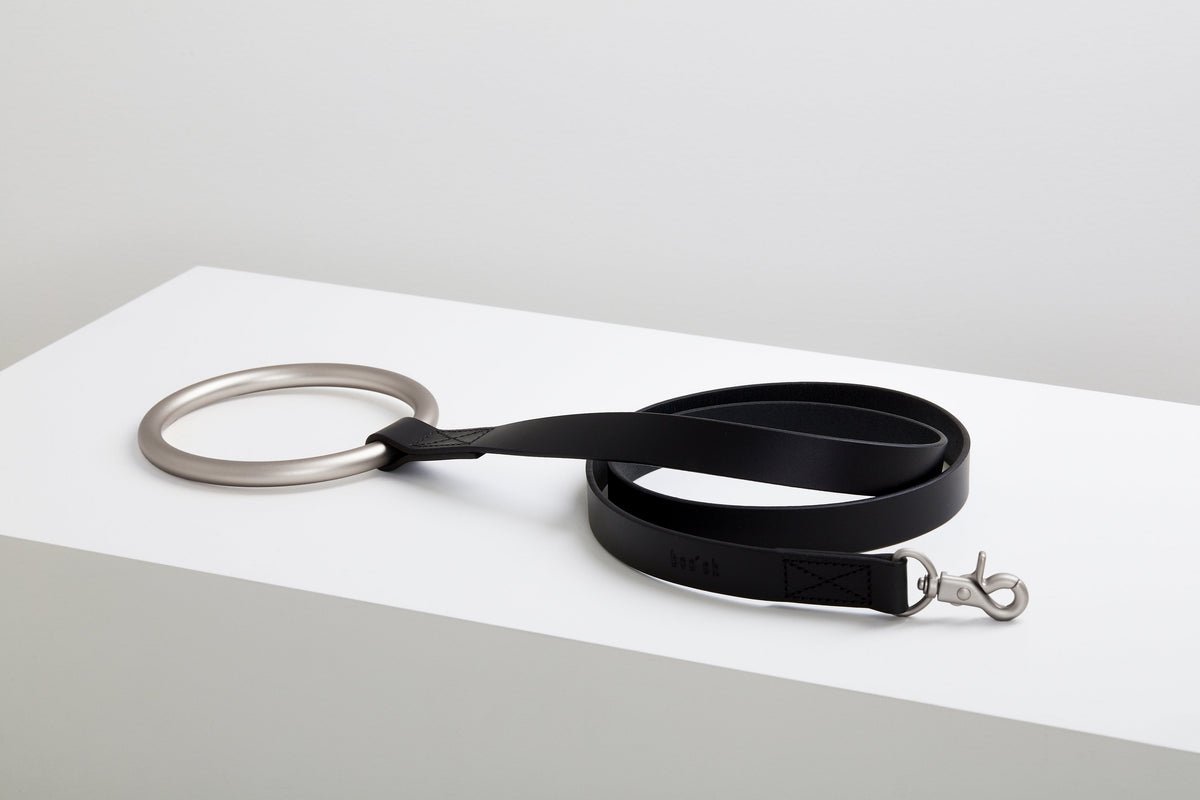 Black Lumi Leash coiled on a raised white display block with its polished clasp and large silver ring handle visible.