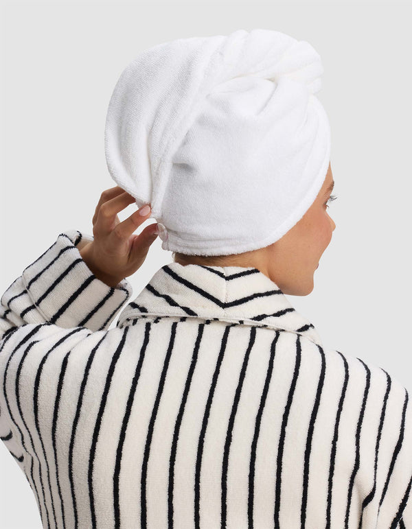 Rear view of the white hair towel wrapped around a model’s head, with one hand adjusting it at the nape above a striped robe.