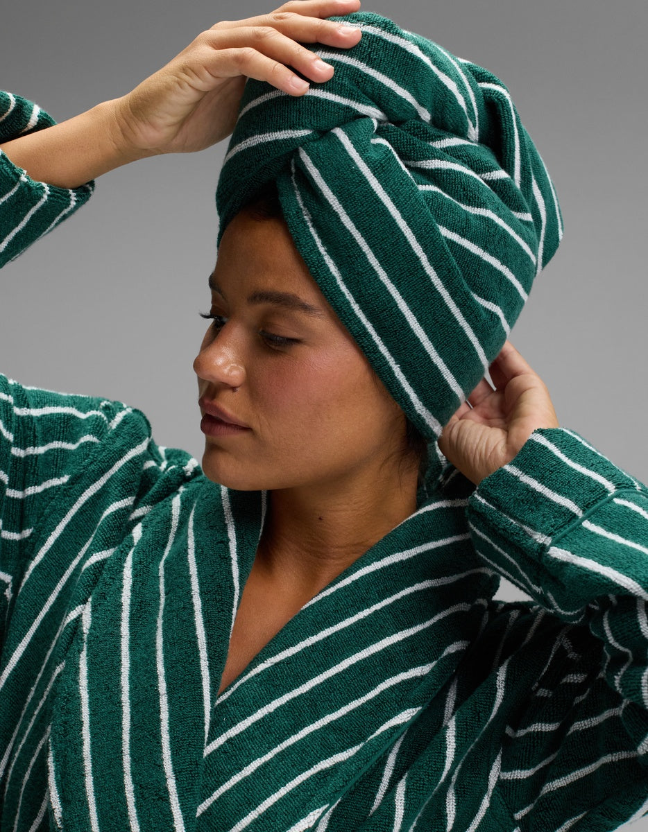Model adjusting a deep green hair towel with narrow white stripes, twisted over her head and paired with a matching striped robe.