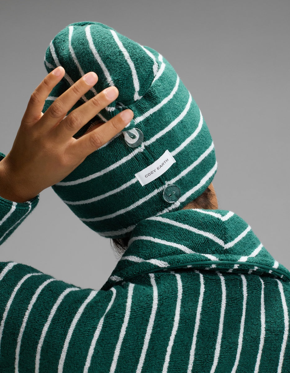 Rear close-up of the green striped hair towel wrap, showing a small white button, fabric label, and the model’s hand resting on top.