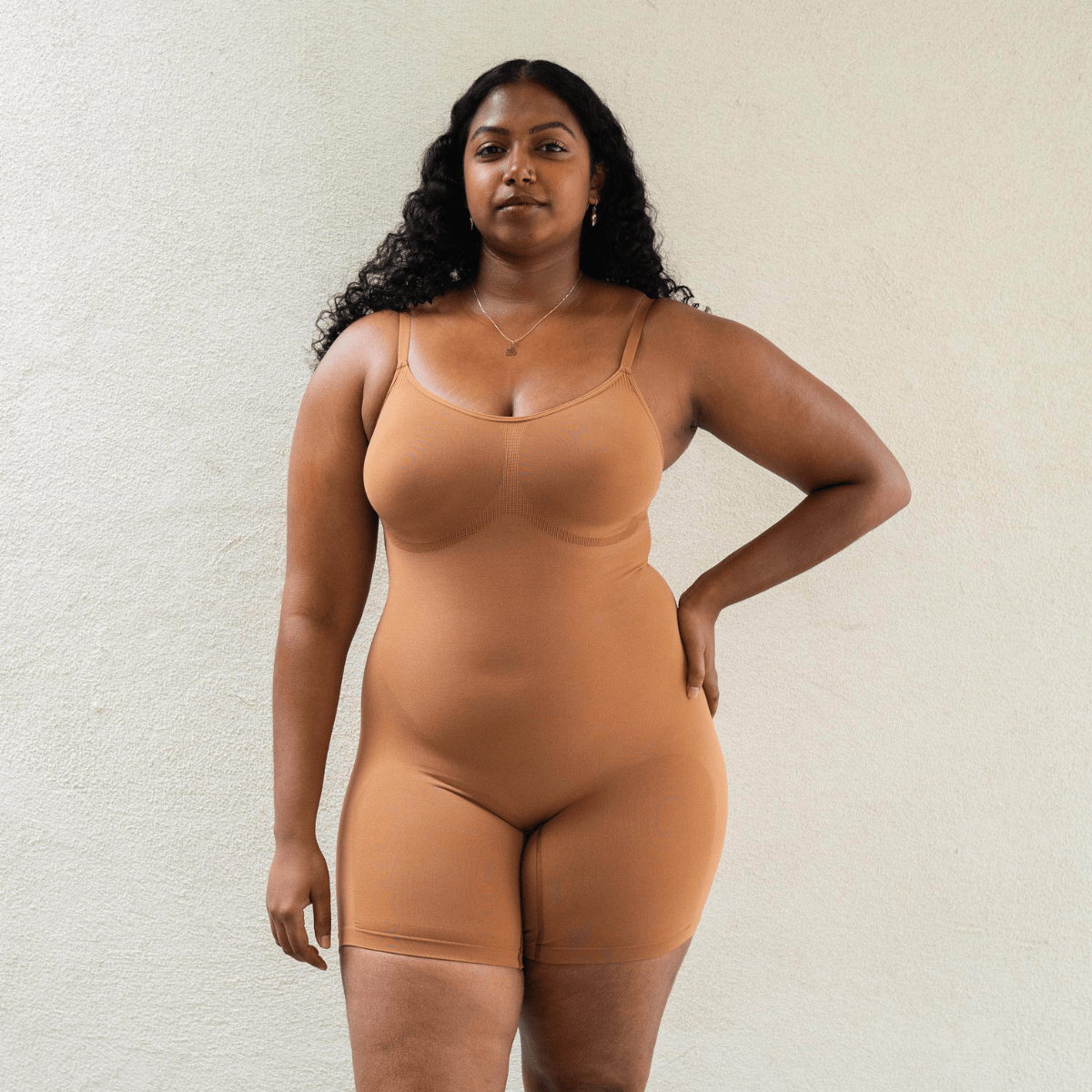 Model wearing PROCLAIM Mid-Thigh Shapewear Bodysuit in Maya Nude, a medium caramel-tone color, front view
