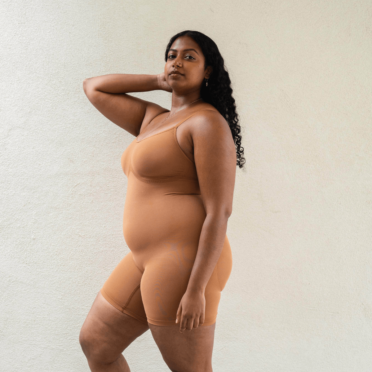 Model wearing PROCLAIM Mid-Thigh Shapewear Bodysuit in Maya Nude, side view