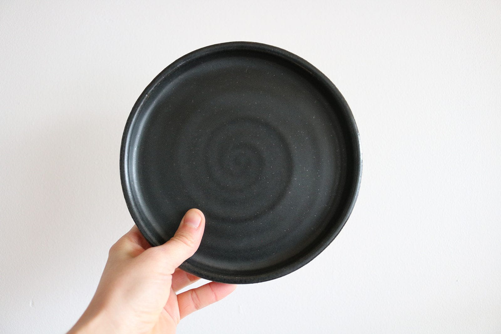 Matte black handmade ceramic small plate held in hand