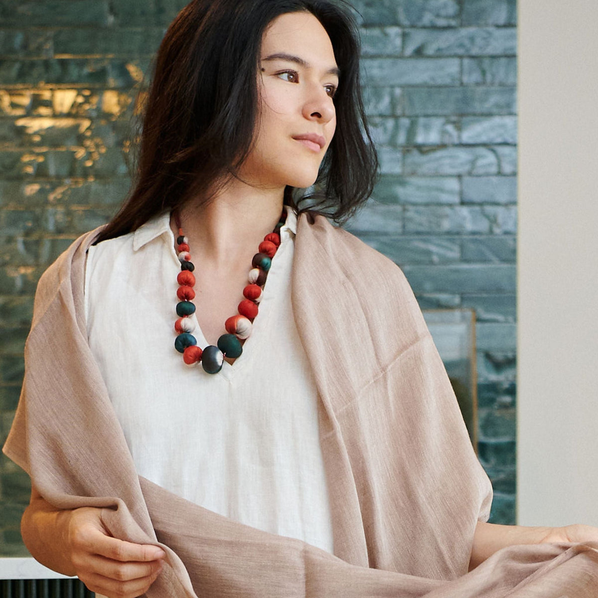 Woman wearing the Jute Golden Brown scarf over a white dress with a colorful statement necklace