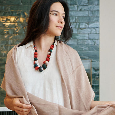 Woman wearing the Jute Golden Brown scarf over a white dress with a colorful statement necklace