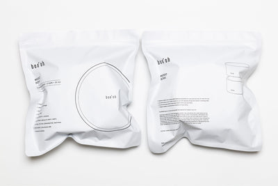 Two white drawstring storage bags printed with Boo Oh product information and simple bowl illustrations.