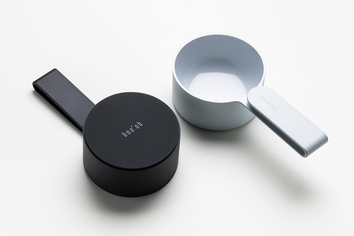Black and pale blue-gray Mogo Scoopers arranged together, showing their contrasting finishes and compact cup-and-handle design.