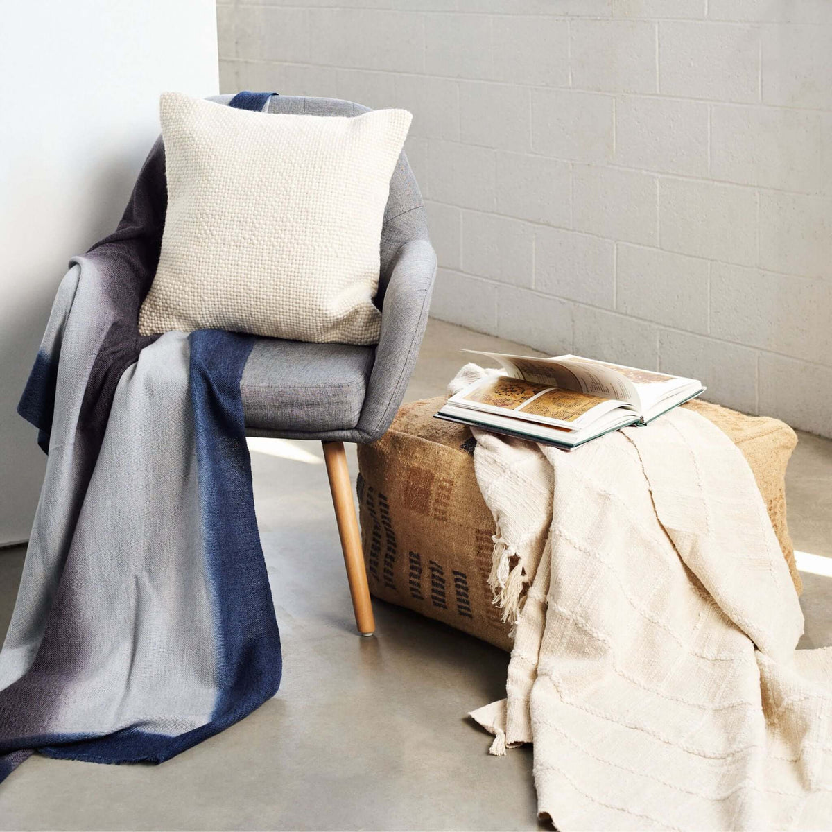 Sea Shell White check-pattern throw layered with blue and cream textiles across an armchair and woven side table