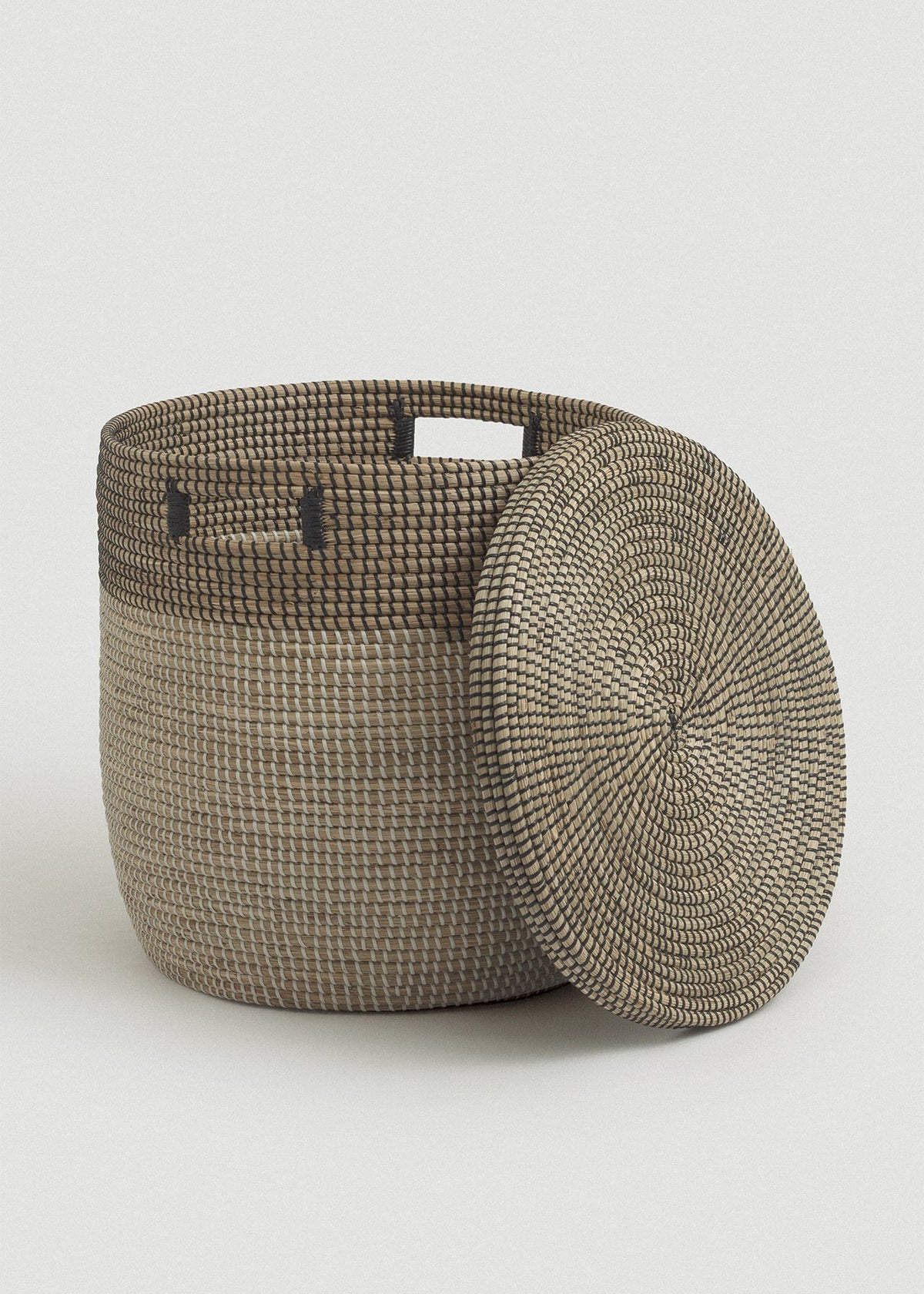 Open seagrass basket with the matching circular lid leaning against its side.