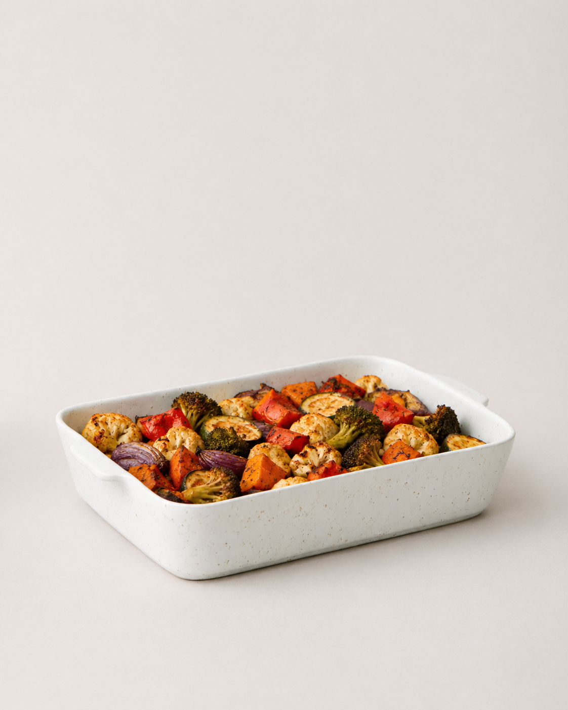 Speckled white Fieldstone Baker filled with roasted vegetables in red, green, orange, and golden-brown tones.
