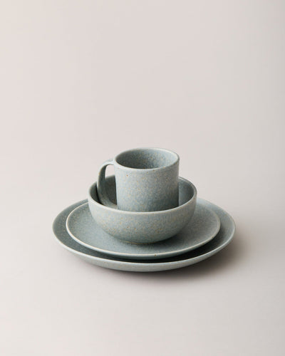 Blue-gray speckled stoneware place setting with a mug nested in a bowl above two stacked plates.