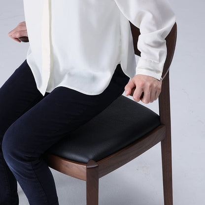 Person sitting on a wooden chair with a black cushioned seat pad. WING Side Chair by CondeHouse
