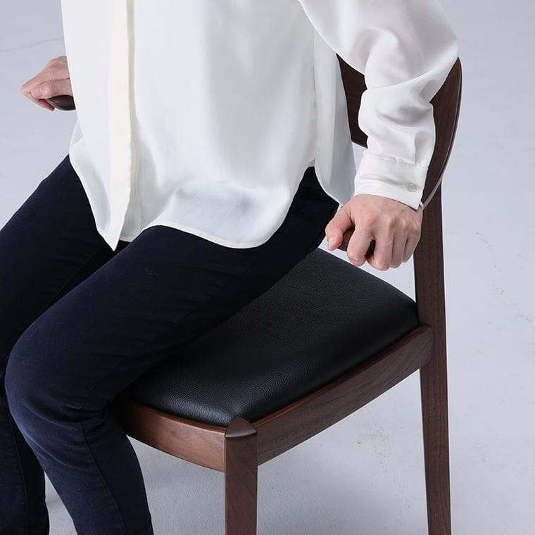 Person sitting on a wooden chair with a black cushioned seat pad. WING Side Chair by CondeHouse