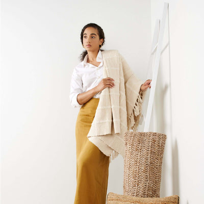 Woman displaying the Sea Shell White handloom throw over one arm, showing its raised checks and long knotted fringe