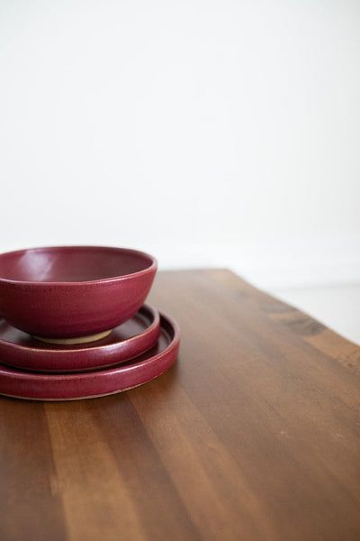 Red glazed handmade bowls and plates stacked on wood surface