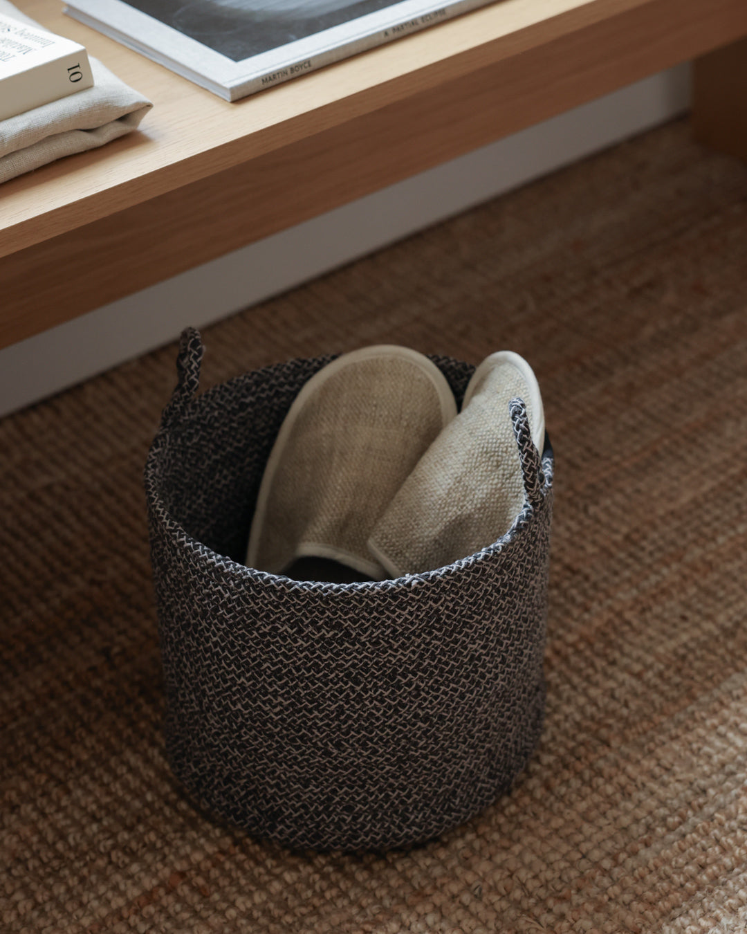 Small gray rope basket holding slippers beneath a low wooden shelf.