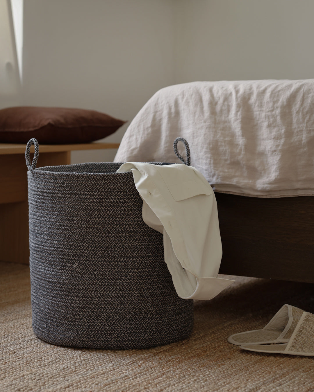 Large gray rope basket beside a bed with a cream textile hanging over the rim.