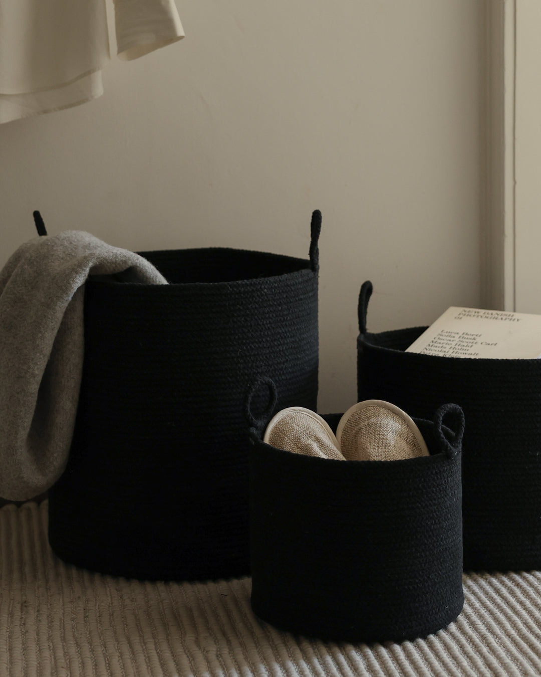 Three basket sizes used to organize blankets, yarn, and reading materials in a neutral interior.