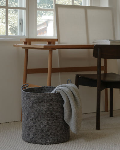 Large gray melange basket with a soft throw draped over the rim in a bright workspace.