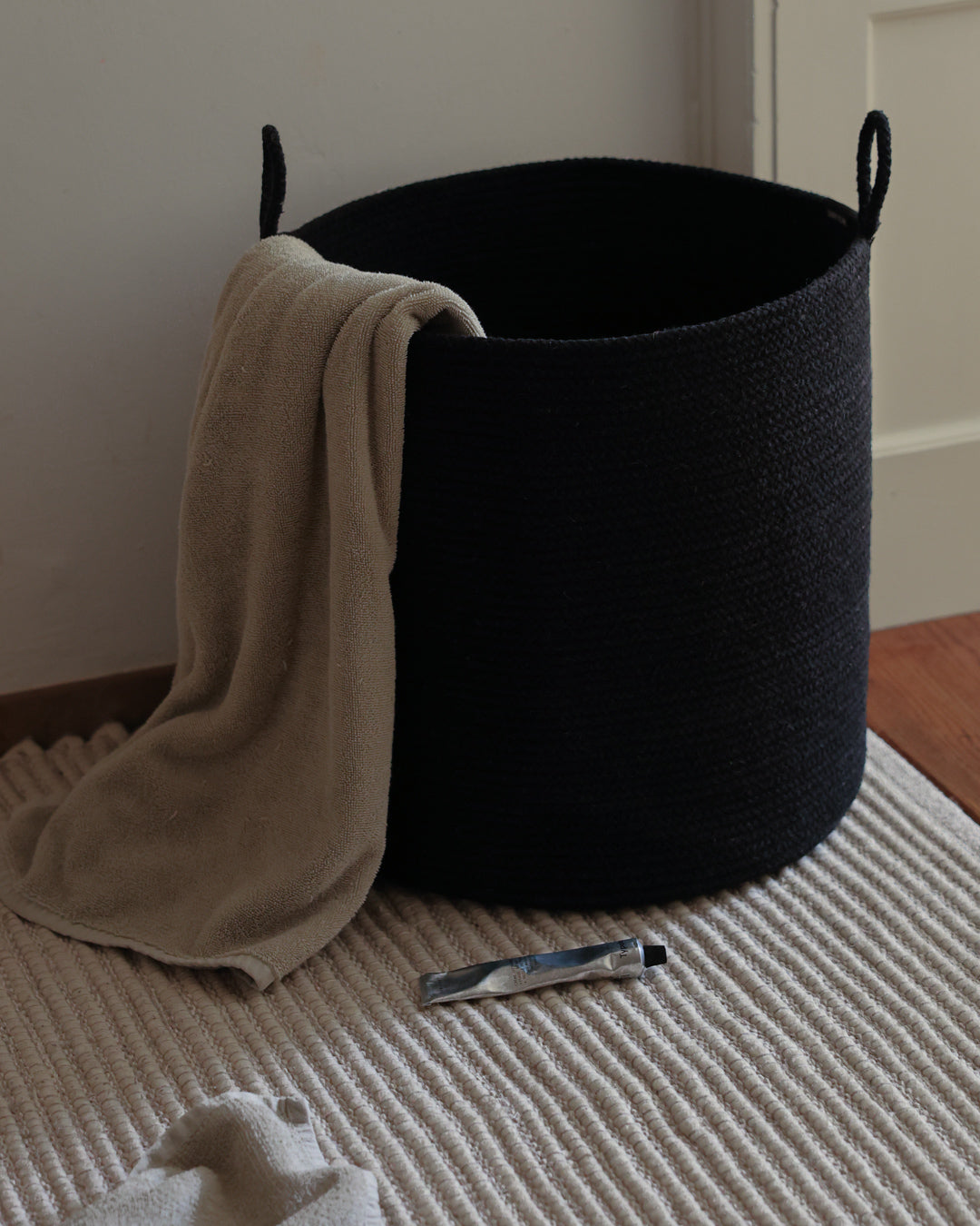 Tall Black Loops basket styled as a laundry hamper with a beige throw draped over its rim.