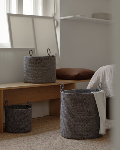 Three basket sizes arranged around a wooden bench in a softly lit bedroom.
