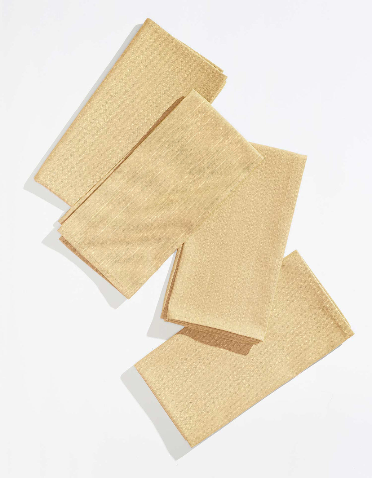 Four mustard-yellow Tortuga Forma Dinner Napkins Sabi arranged in overlapping rectangular folds on white, showing their subtle woven texture and neatly finished borders.