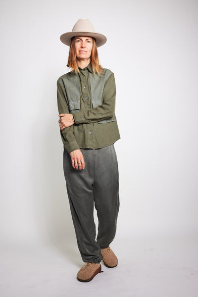 Model standing with folded arms in the olive Trek Shirt, gray pants, and beige hat.