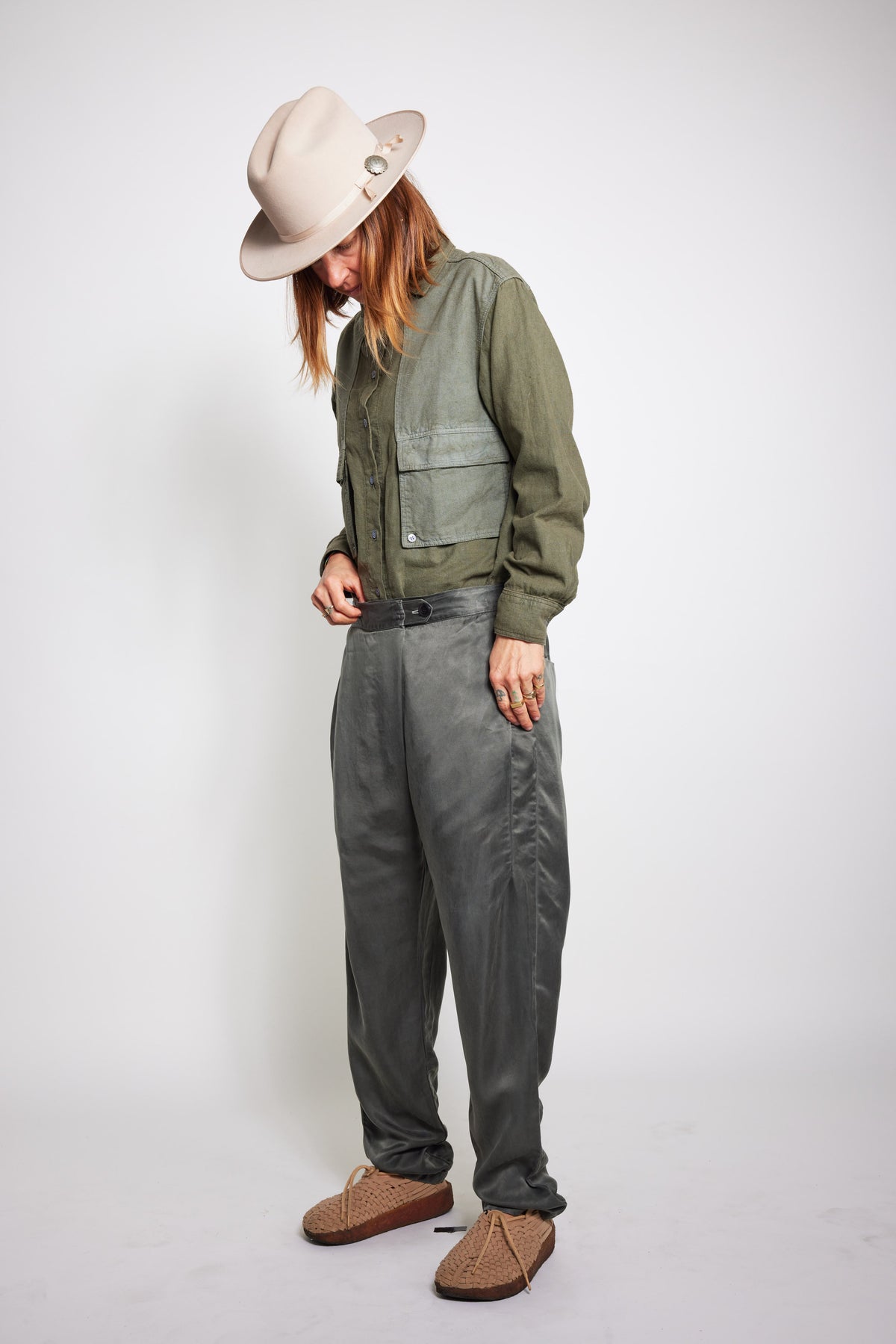 Model looking down while wearing the olive Trek Shirt with gray pants and a beige hat.