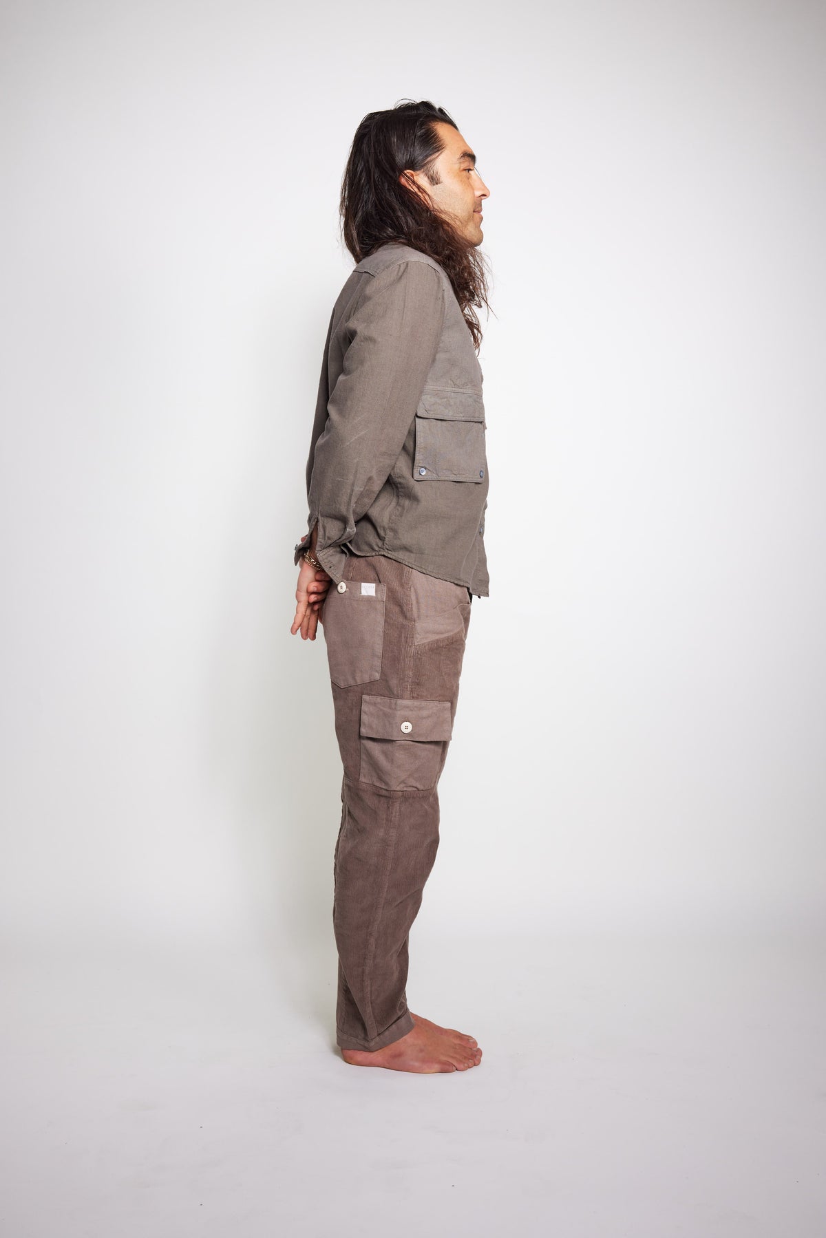 Side view of a barefoot model wearing a taupe-gray Trek Shirt with matching utility pants.