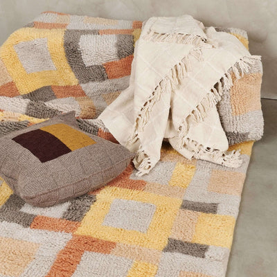 Sea Shell White handloom throw loosely arranged over a multicolored geometric rug, highlighting its neutral color and textured weave