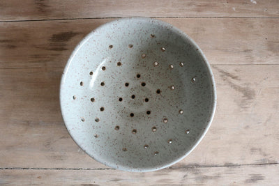 Speckled ceramic colander on a wooden surface